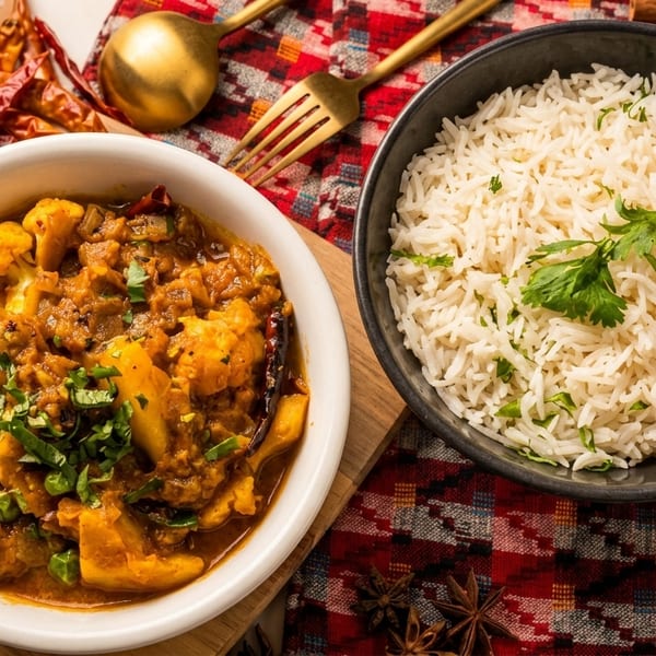 A bowl of cauliflower and potato curry with a side of white rice, garnished with cilantro.