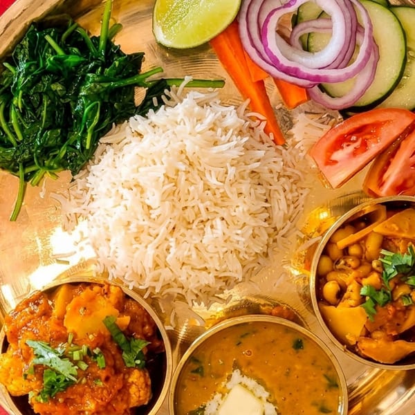 A Nepali thali with rice, dal, vegetables, and curries on a golden plate with cutlery.